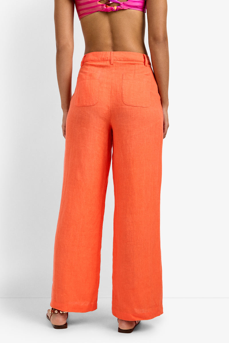 A person faces away, wearing the Tonga Pant in bright orange with back pockets and a pink crop top, creating a summery, stylish look against a plain white background.