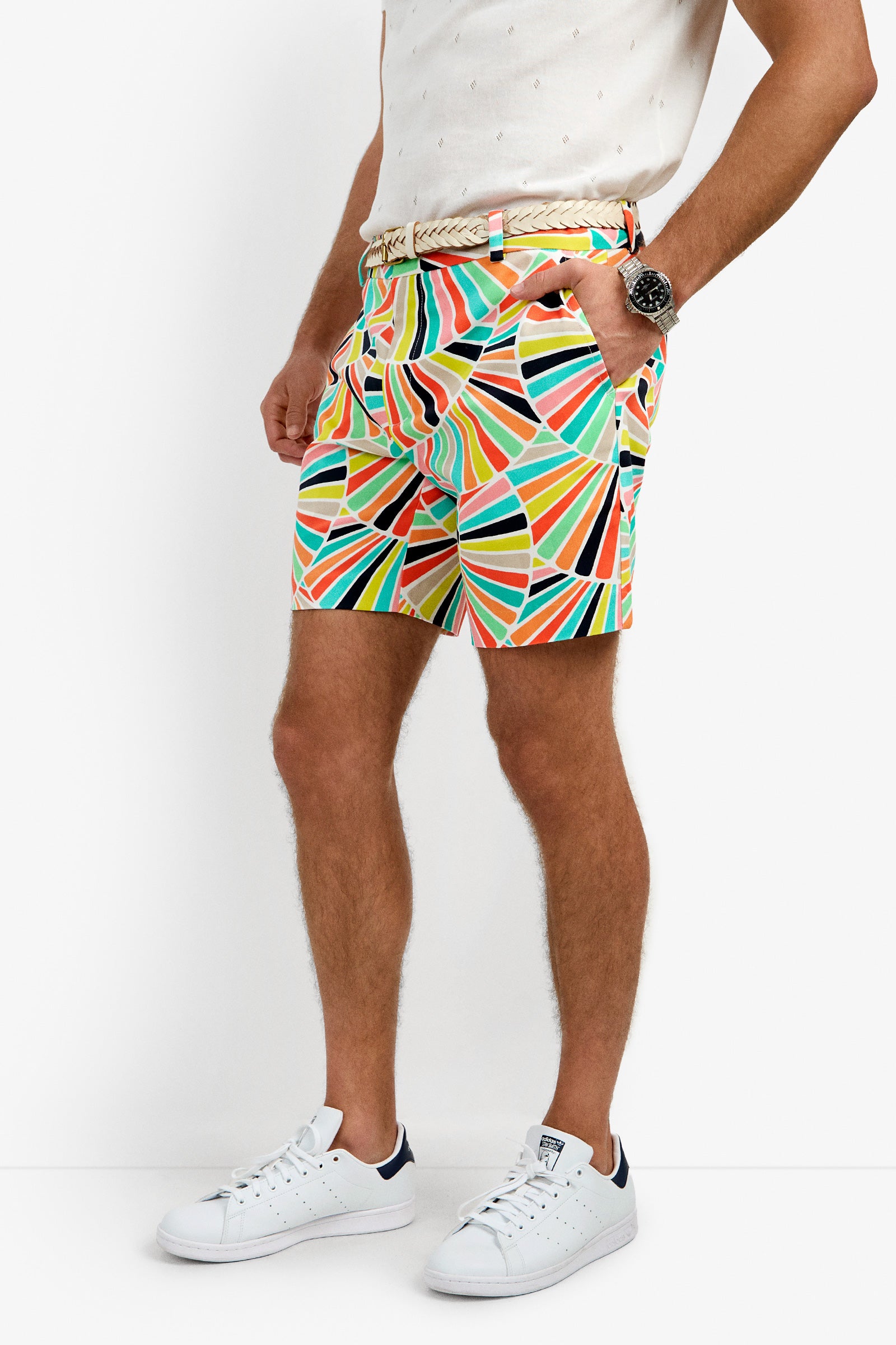 A man stands against a white background wearing the Lawrence Short, featuring a colorful geometric pattern, paired with a white textured shirt, woven belt, watch, and white sneakers with dark accents.