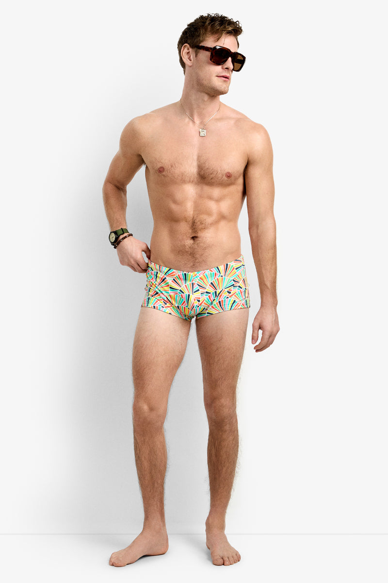 A man in Sorrento Swim Trunk, color MULTI, stands barefoot against a plain white background, looking to his left with one hand on his hip and wearing large sunglasses.