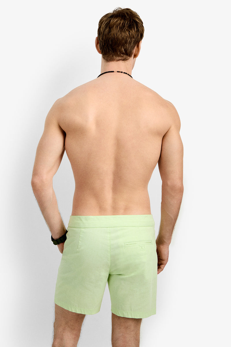 A shirtless, light-skinned man with brown hair stands facing away in Honolulu Board Short (light green) and a black wristband, set against a plain white background.