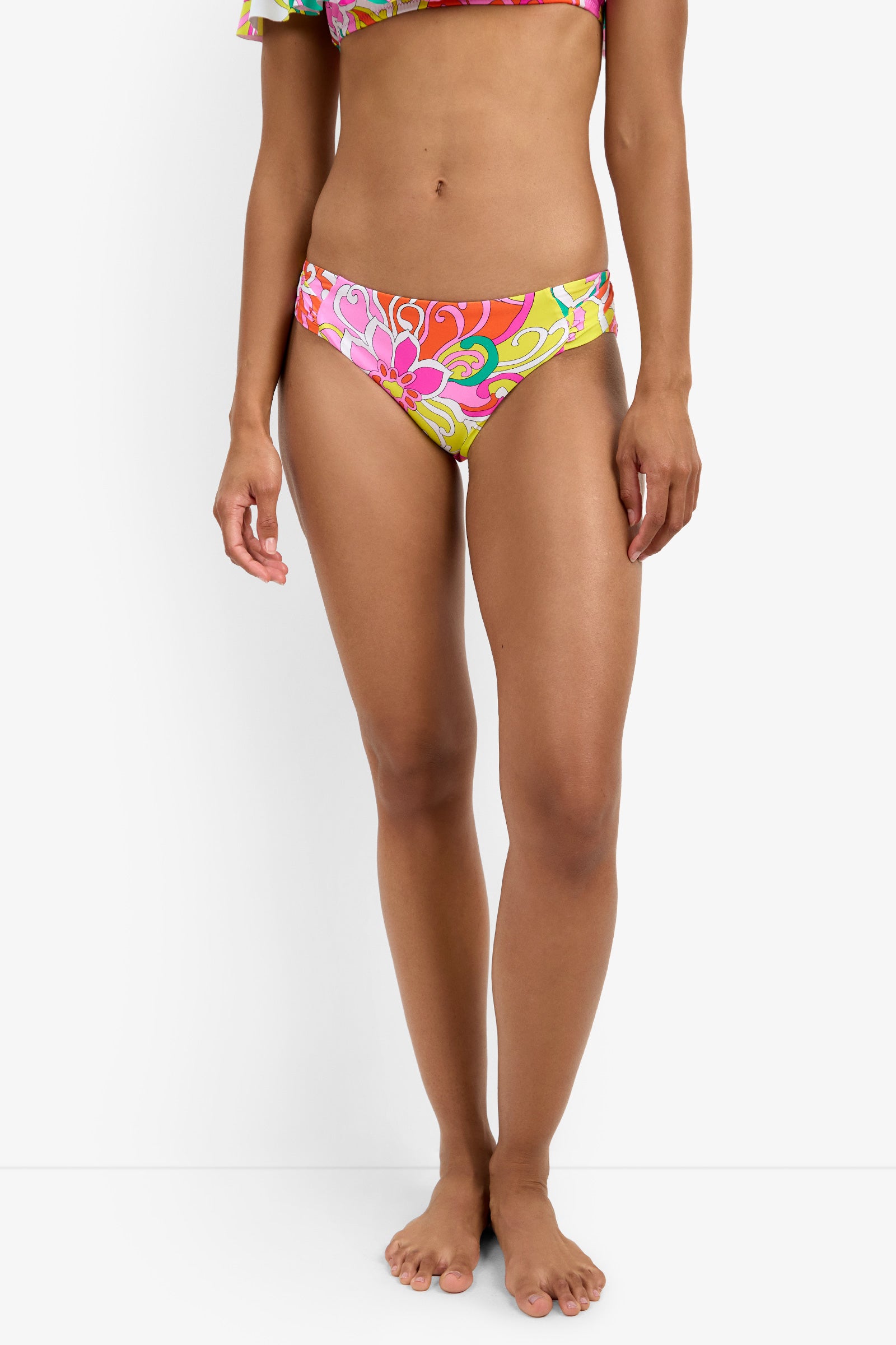 A woman stands barefoot against a white background, wearing Shirred Hipster Swim Bottoms with a colorful floral pattern and a matching bikini top partially visible. Her arms rest relaxed at her sides.