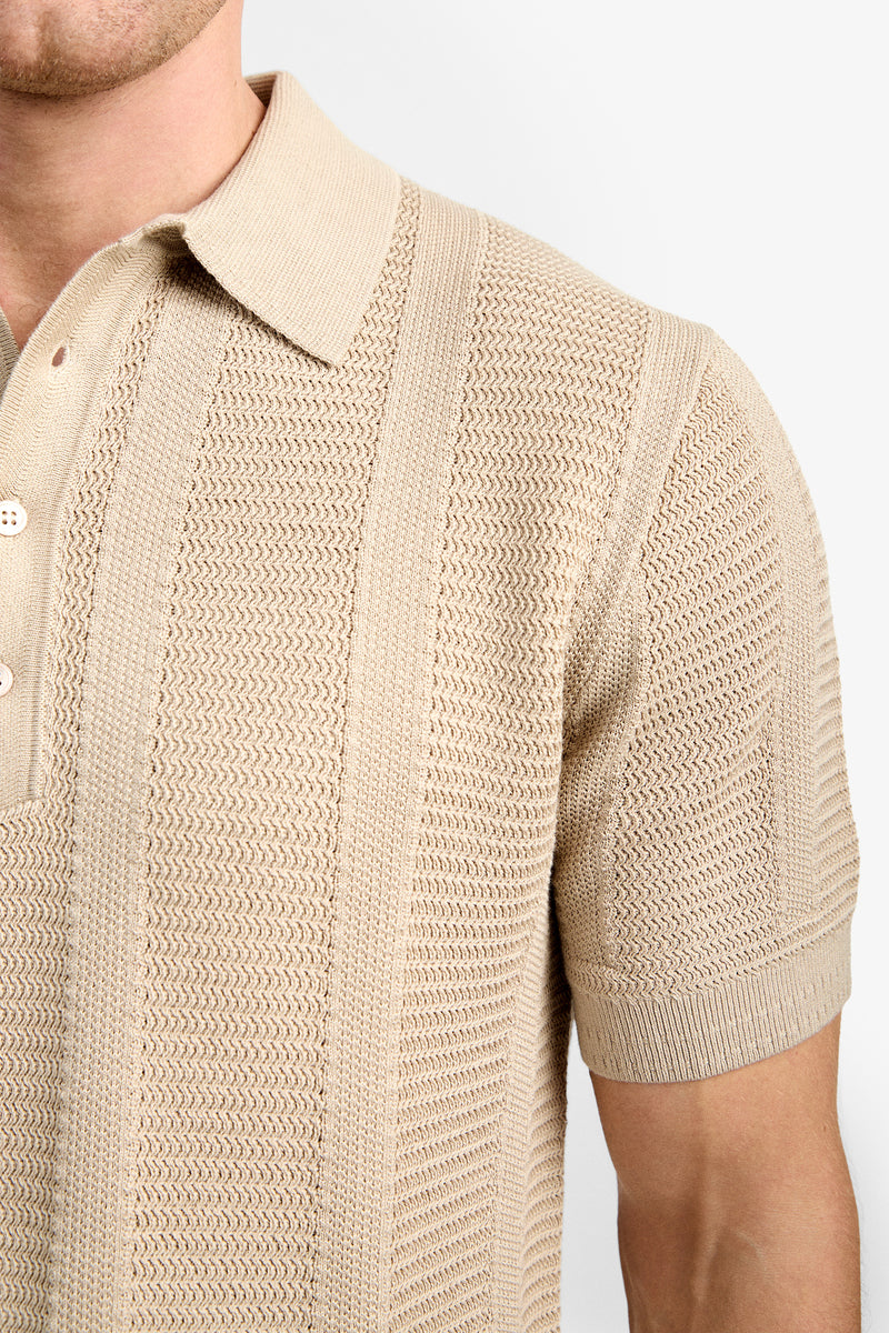 A close-up of a person wearing the Devan Short Sleeve Polo, a beige knit shirt with a collar and buttons, highlighting the textured pattern of the fabric.