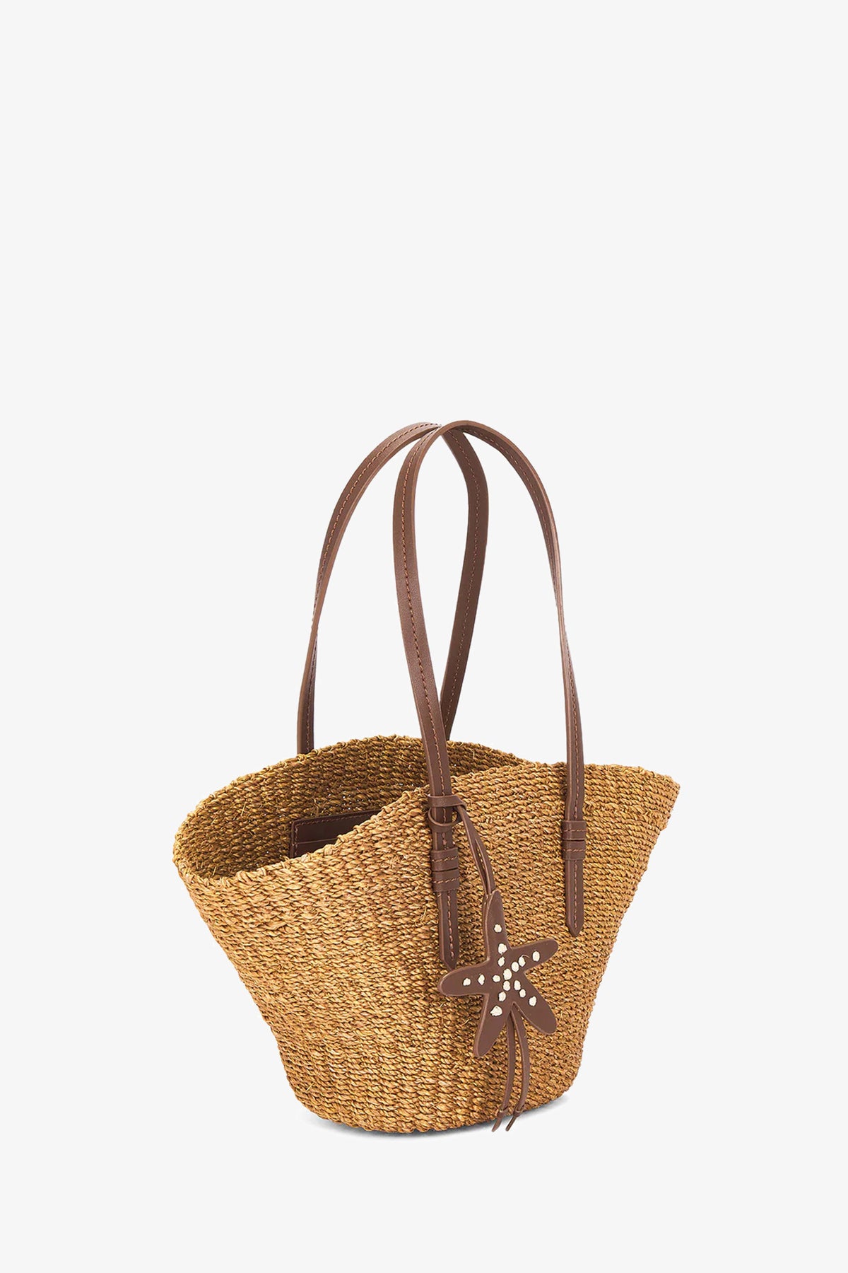 The East West Mini Tote is a woven straw bag with two brown leather shoulder straps and a starfish-shaped leather charm on one handle, shown against a plain white background.