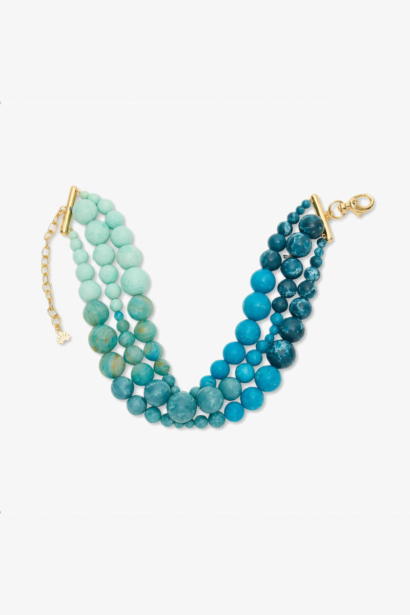 The Riviera Diana Triple Row Necklace features multiple strands of round blue and turquoise beads with a gold clasp and extender chain, displayed on a white background.