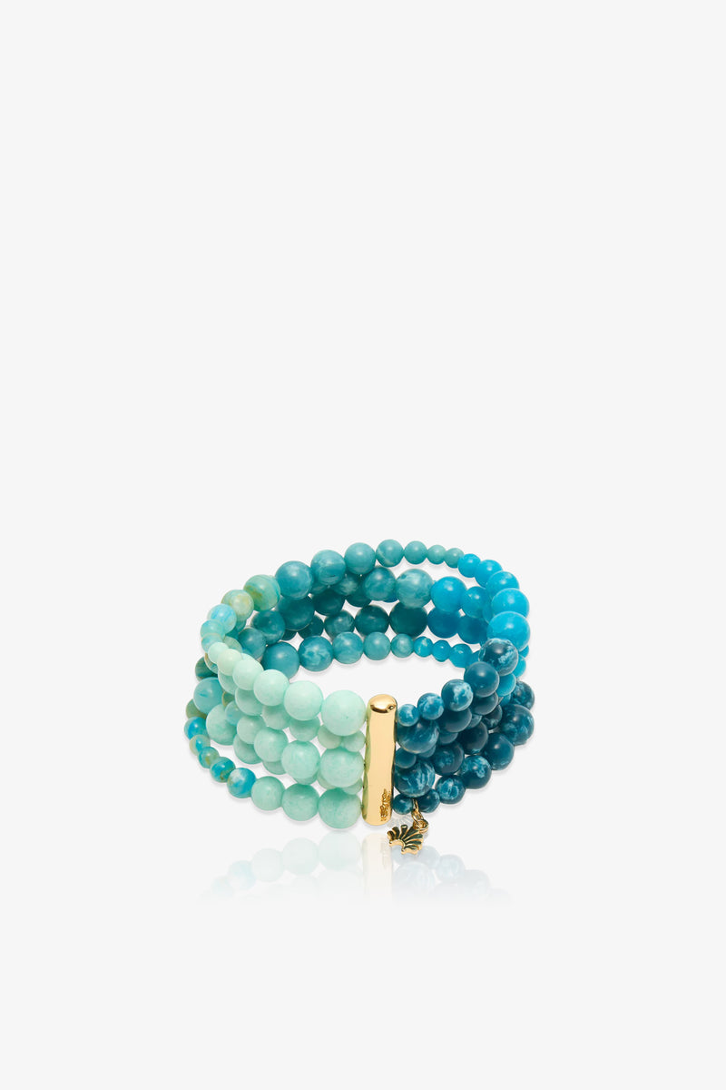 The Riviera Five Strand Bracelet features round beads in shades of blue and green across multiple strands, accented by a gold rectangular bar and a small gold charm, and is displayed on a white background.