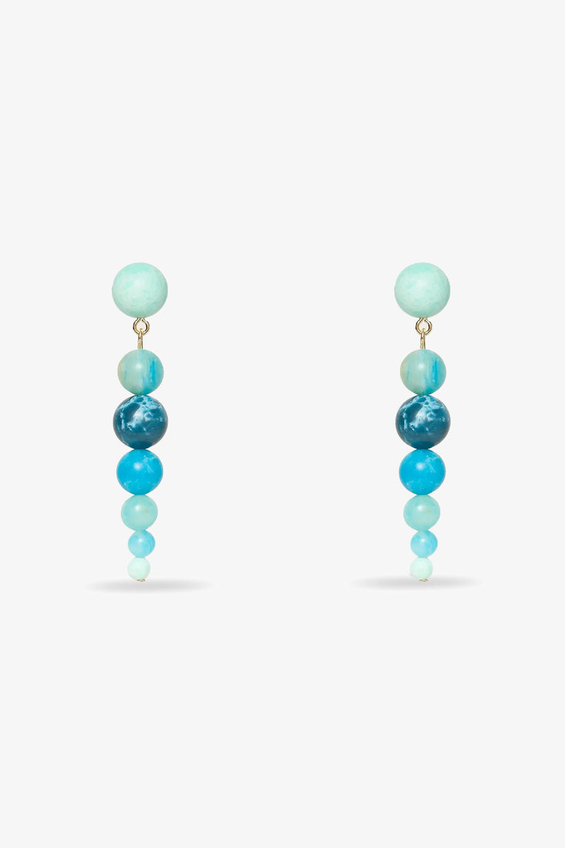 The Riviera Linear Drop Earrings feature five round beads each, arranged largest to smallest in gradient blue and turquoise hues, displayed on a white background.