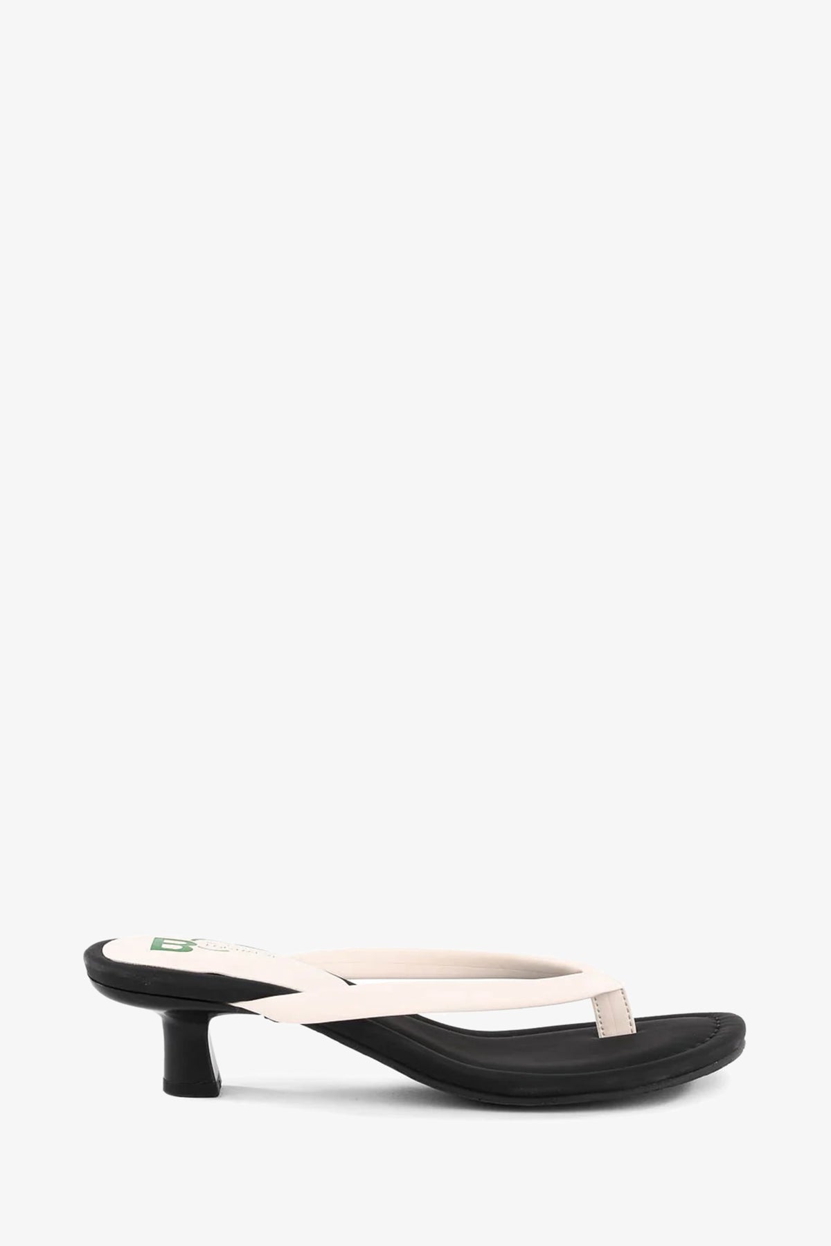 Riptide Sandal: cream leather thong sandal featuring a black kitten heel and black footbed, shown in side view on a white background.