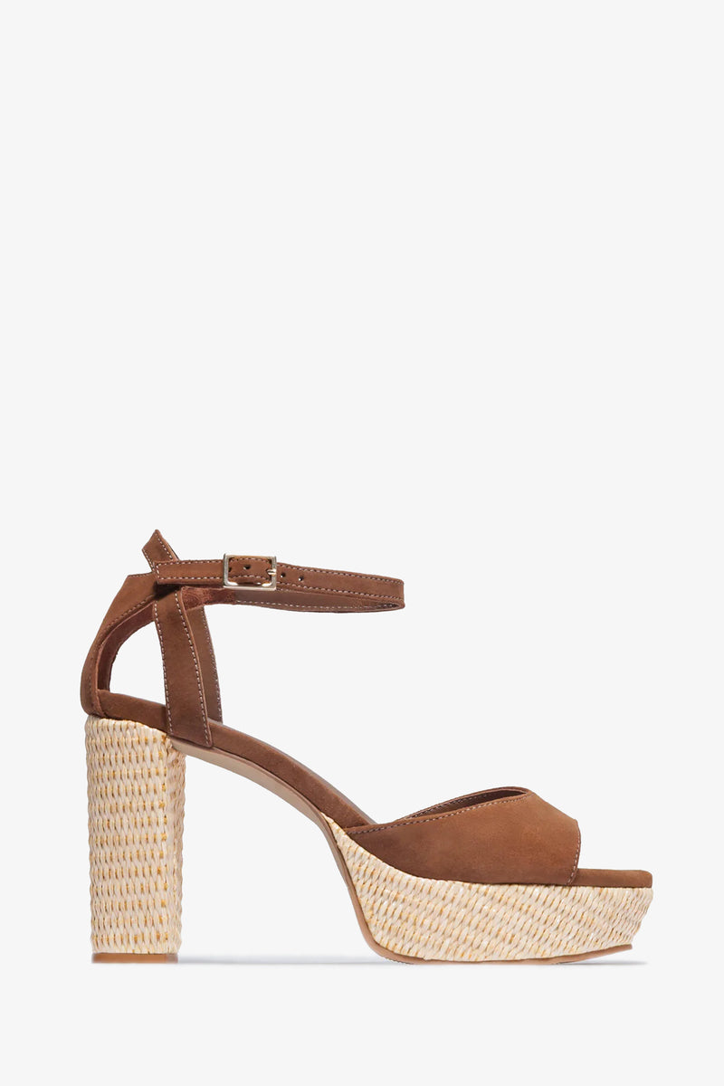 The Valeria Platform Sandal features brown suede, an open toe, ankle strap with buckle closure, and a high block heel with a woven textured platform. Displayed against a plain white background.