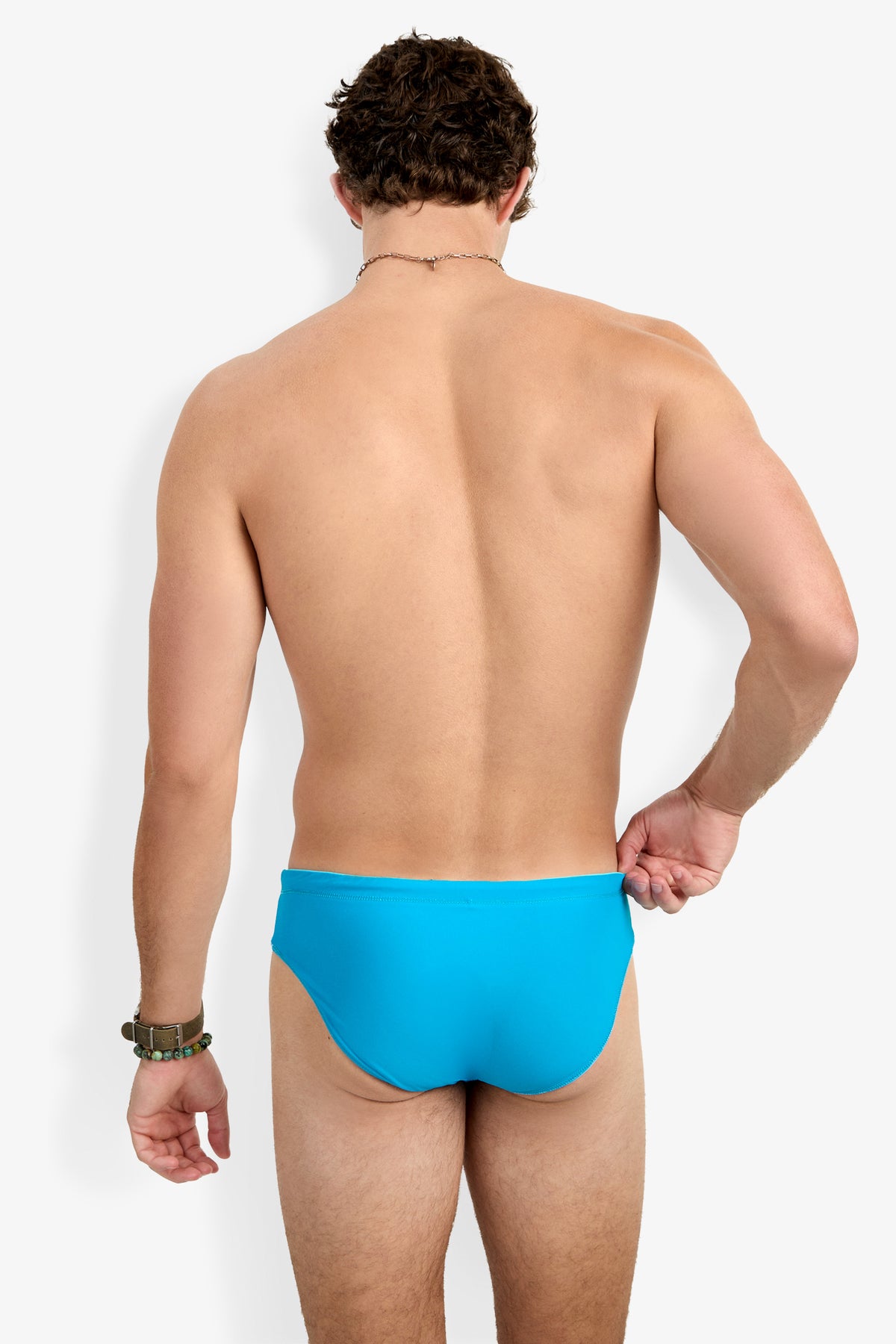 A man, shown from the back against a plain white background, wears the Palm Beach Swim Brief in bright blue and holds its side with one hand.