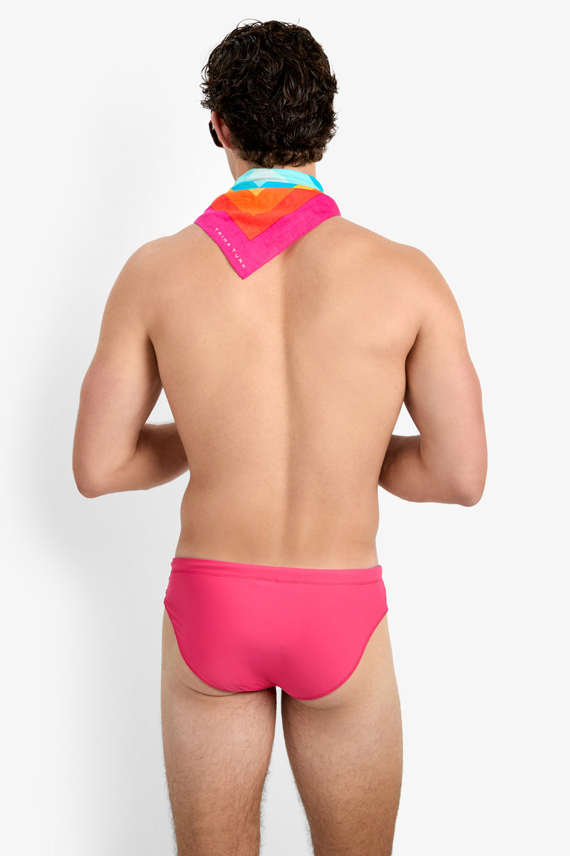 A man with curly brown hair stands facing away, wearing the Palm Beach Swim Brief and a colorful scarf, his back visible against a plain white background.