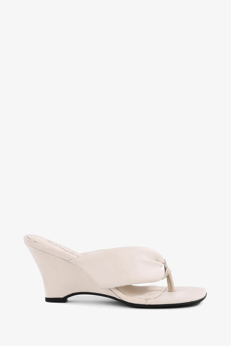The Wishing Well Wedge: a single cream-colored sandal featuring an open toe, thong strap, and low angled wedge heel, displayed against a plain white background.