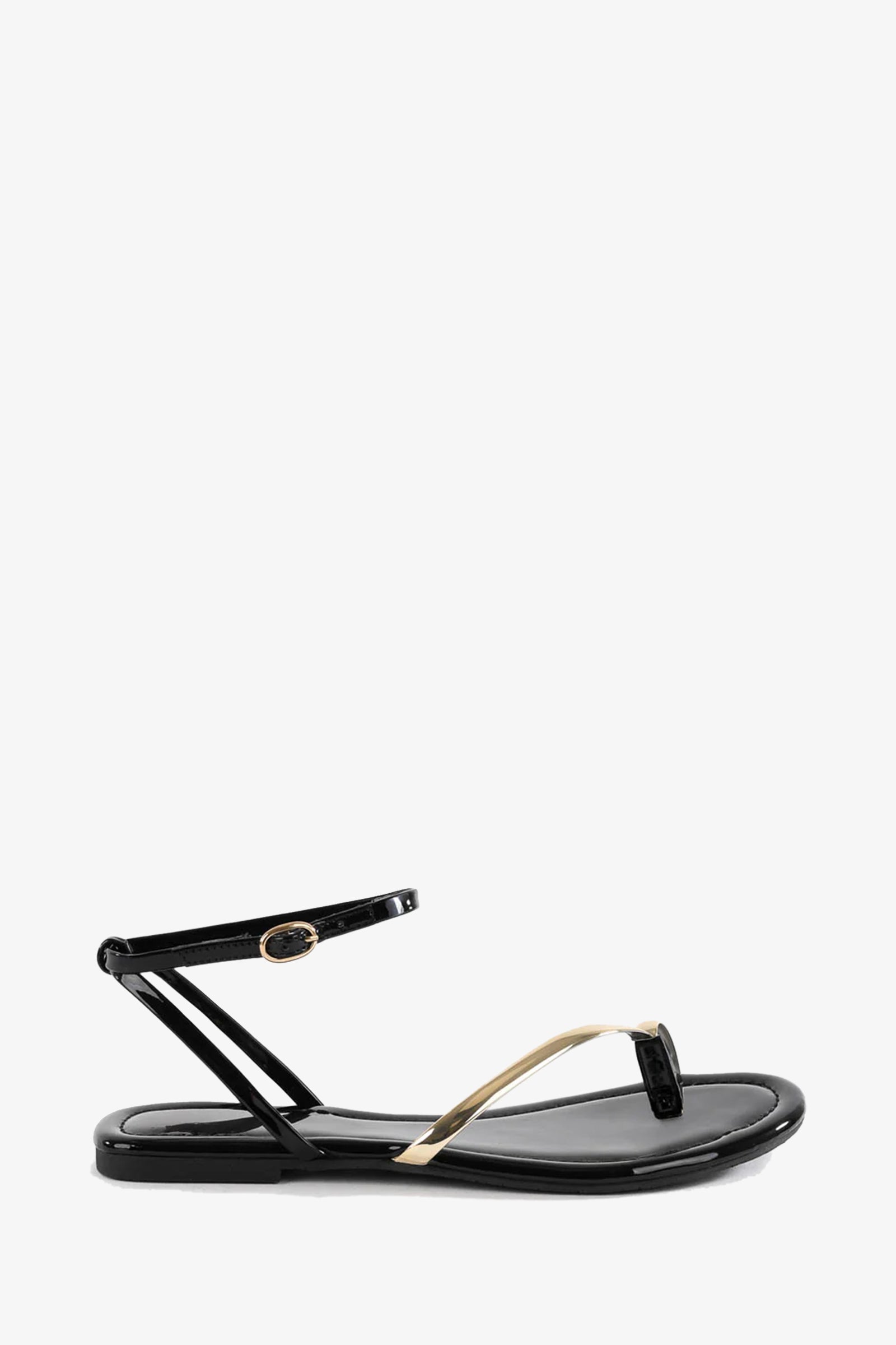 The A Little Extra Sandal is a sleek black flat with a thin ankle strap, simple thong design, and metallic gold accent on the front strap, shown against a white background.