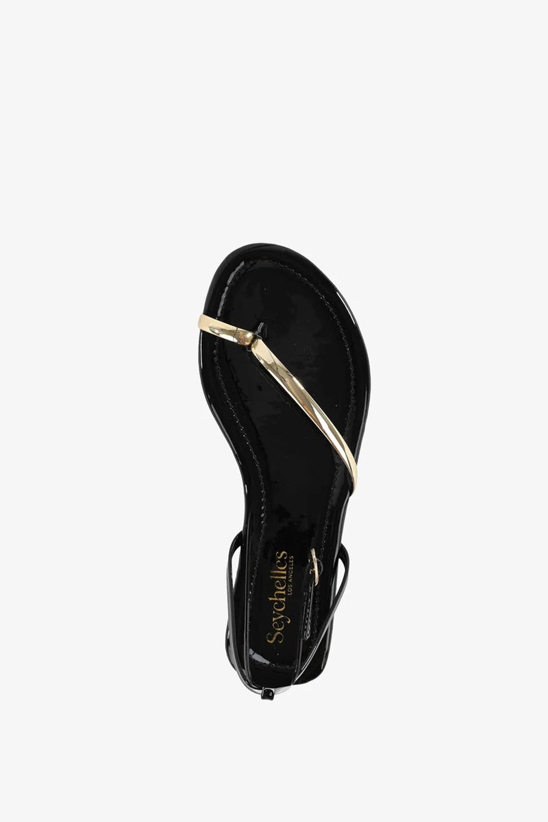 A black A Little Extra Sandal featuring a thin metallic gold strap crossing over the toes and foot, viewed from above on a white background. The sole displays Seychelles branding near the heel.