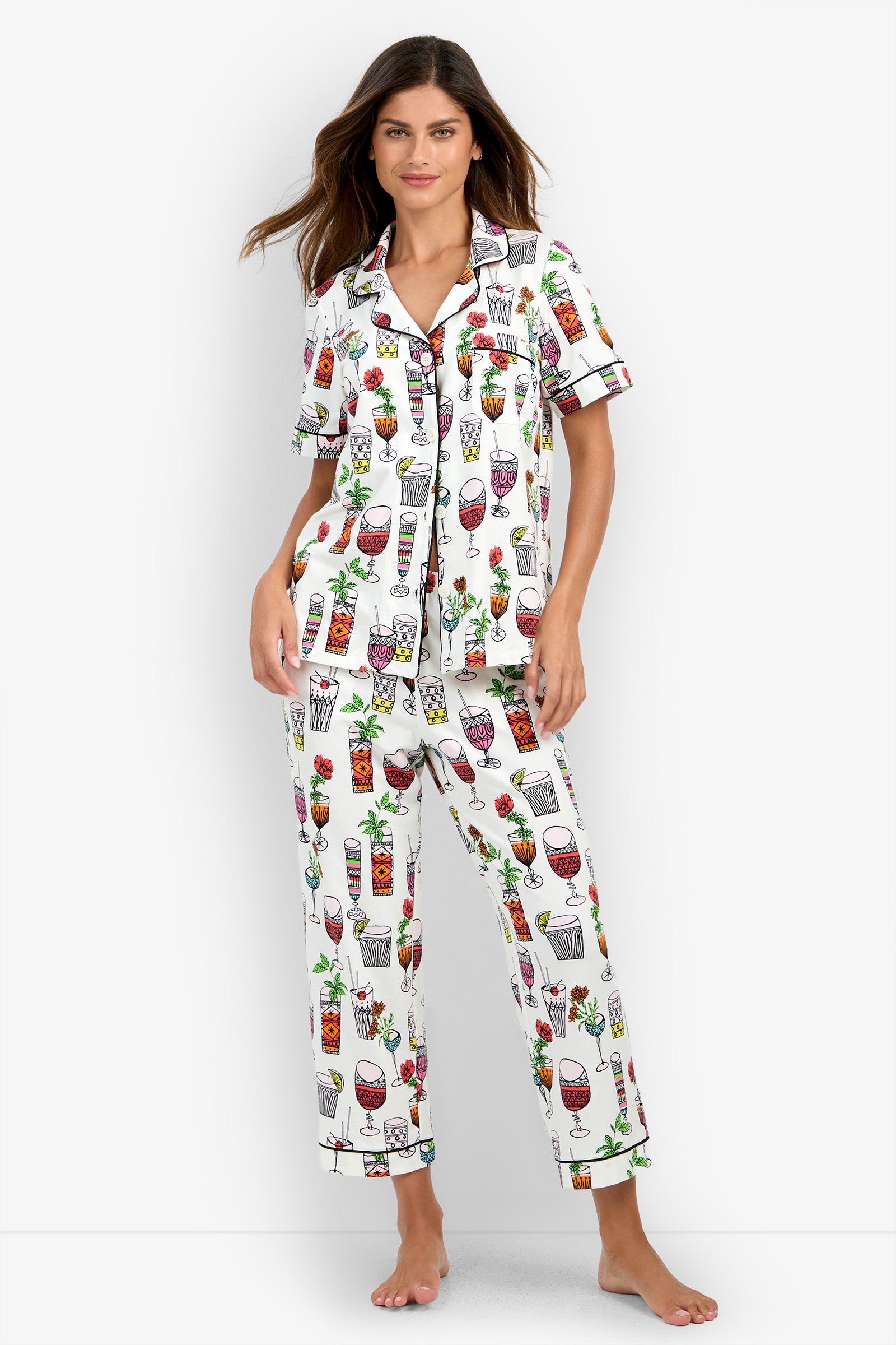 A woman models the Short Sleeve Cropped Pajamas Set, featuring a white fabric with colorful drink and cocktail glass prints, as she stands barefoot against a plain background and looks at the camera.