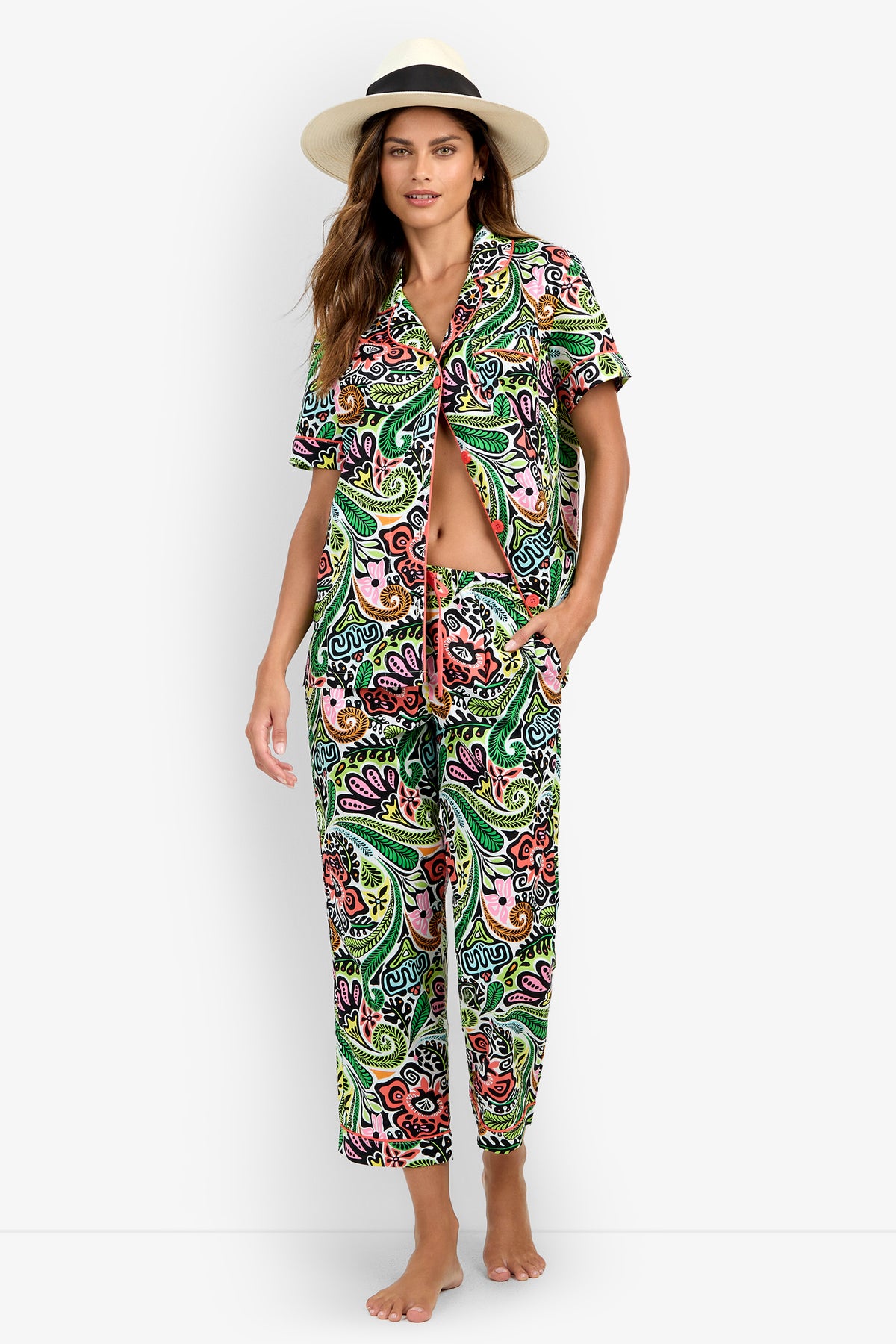 A woman wearing the Short Sleeve Cropped Pajamas Set—a colorful, paisley-patterned matching shirt and pants ensemble—with a beige hat, stands barefoot against a white background.