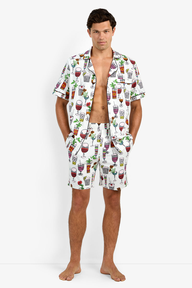 A man stands barefoot with his hands in his pockets, wearing unbuttoned Short Sleeve Boxer Pajamas featuring a vibrant cocktail and drink print on a white background.
