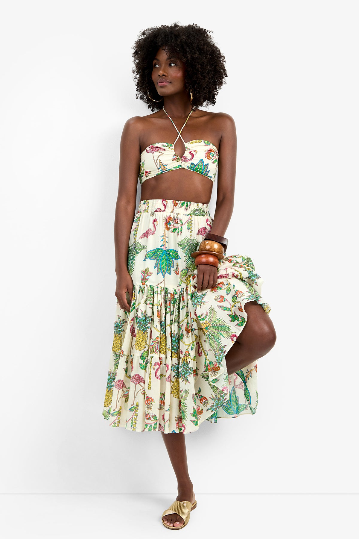 A woman with curly hair wears the Marisalle Top in Flamingo Fizz, paired with large bangles and beige sandals, standing against a plain white background.