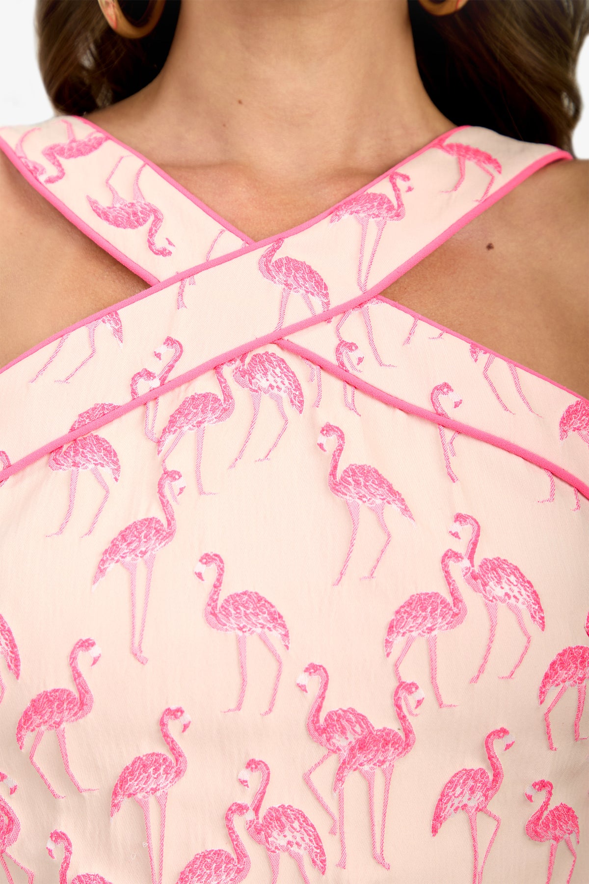 Close-up of the Piped Wanona Top, a light pink garment with crisscrossed straps and an embroidered pink flamingo pattern, highlighting the upper chest and neckline area.