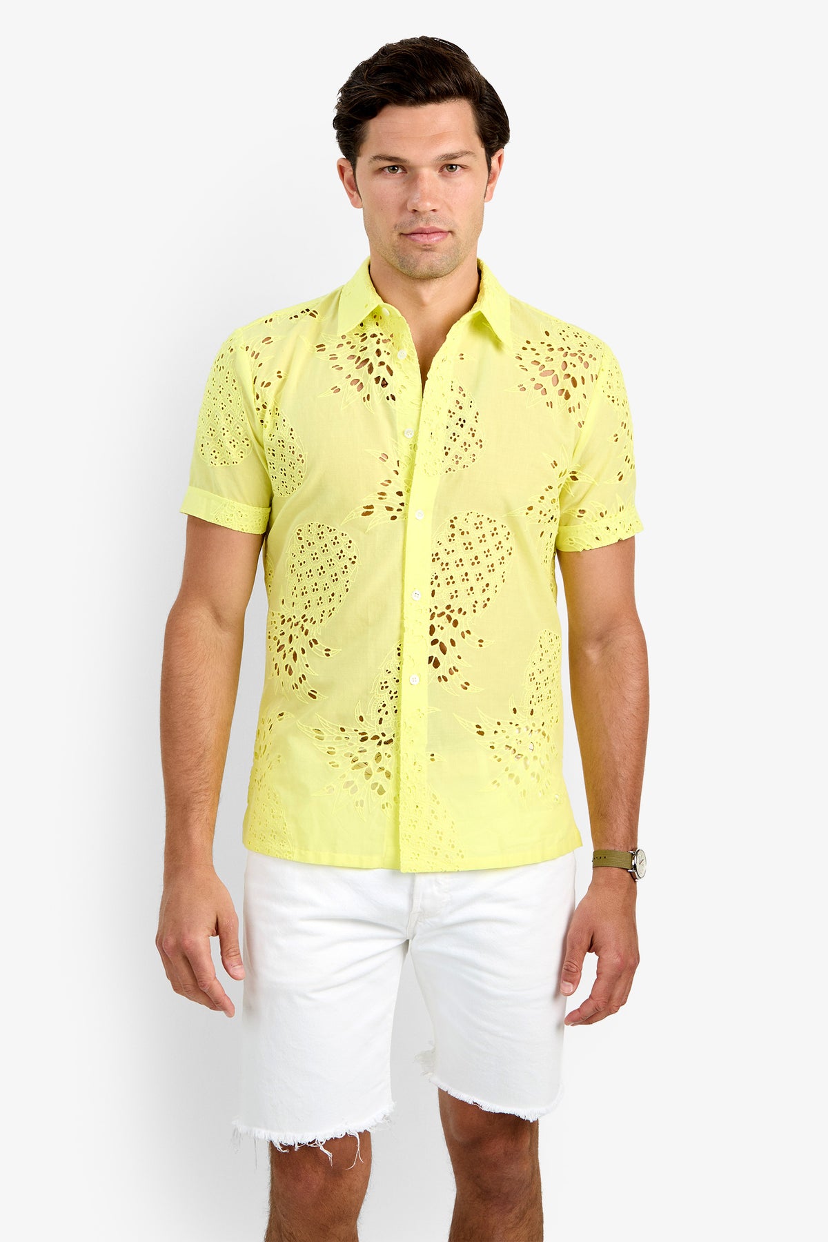 A man wearing the BRANSON SHIRT, a light yellow, short-sleeve 100% cotton button-up with eyelet details, and white frayed hem shorts stands against a plain white background.