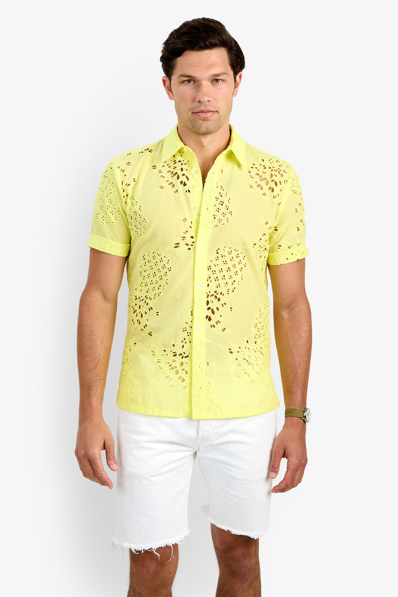 A man wearing the BRANSON SHIRT, a light yellow, short-sleeve 100% cotton button-up with eyelet details, and white frayed hem shorts stands against a plain white background.