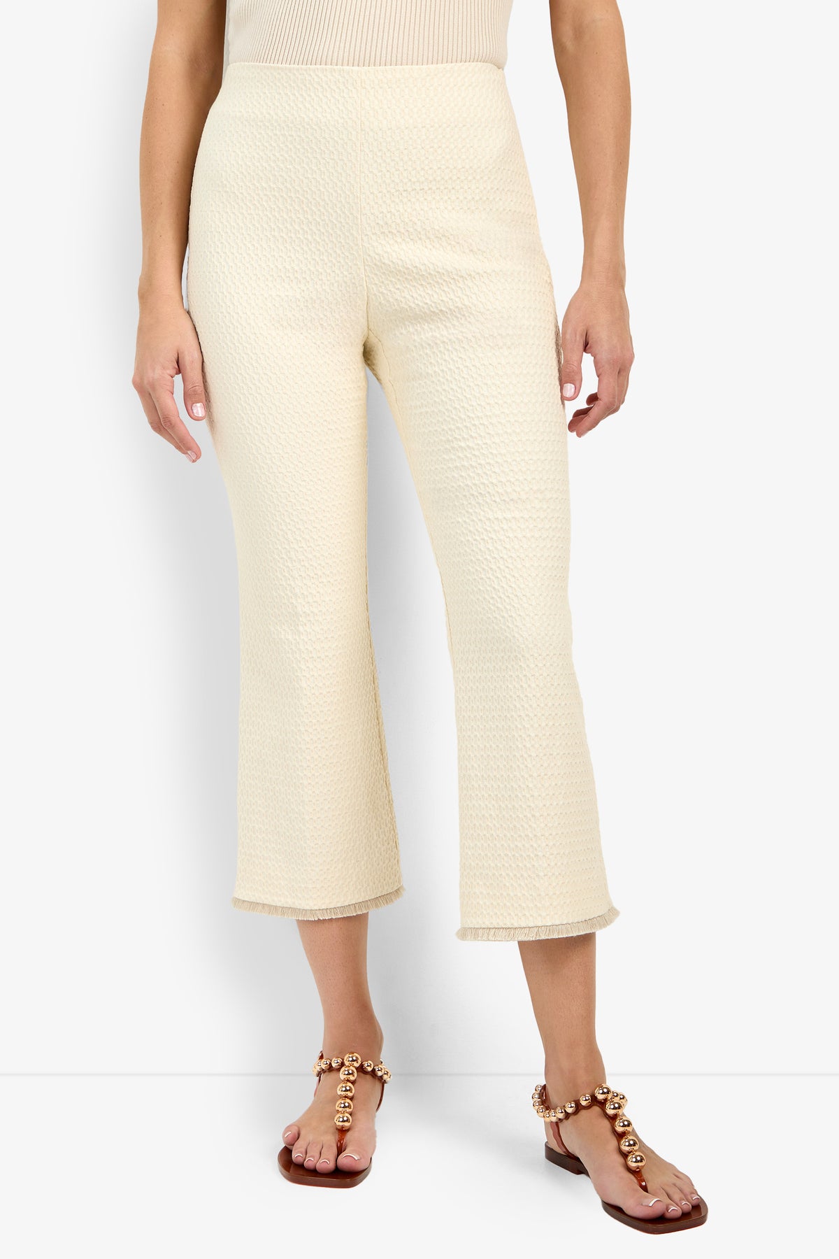 A person wears the Gulf Pant in cream texture, paired with a sleeveless beige top and flat sandals with round gold embellishments, standing against a white background.