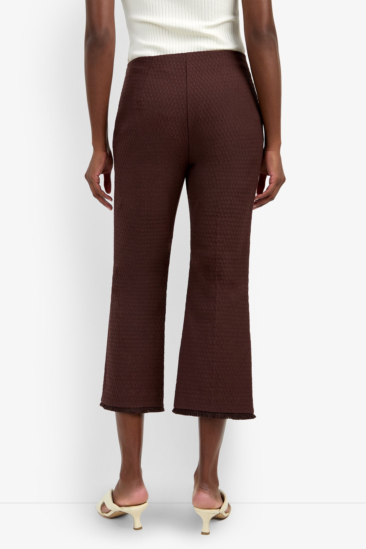 A person wearing the Gulf Pant in a textured brown fabric and cream heeled sandals, standing with their back to the camera. The person is also wearing a sleeveless white top.