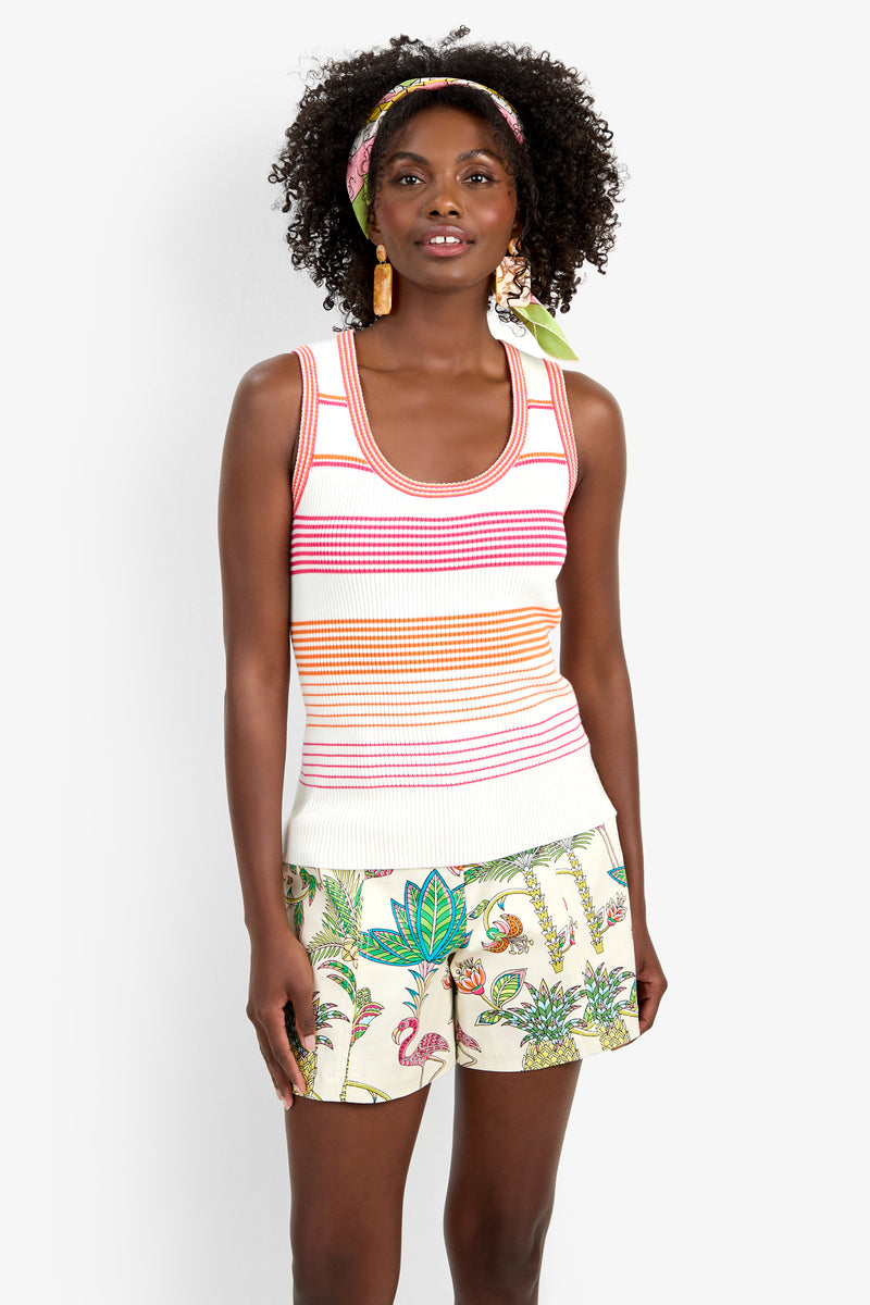 A woman with curly hair, a printed headband, and large earrings smiles while wearing the Paolini Tank and tropical print shorts featuring flamingos, plants, and animals.