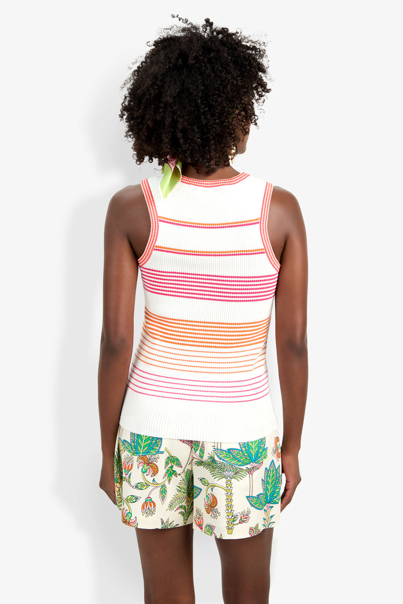 A person with curly hair, seen from behind, wears the Paolini Tank—a sleeveless white knit top with orange, pink, and red stripes—paired with light shorts featuring a colorful floral and leaf pattern.