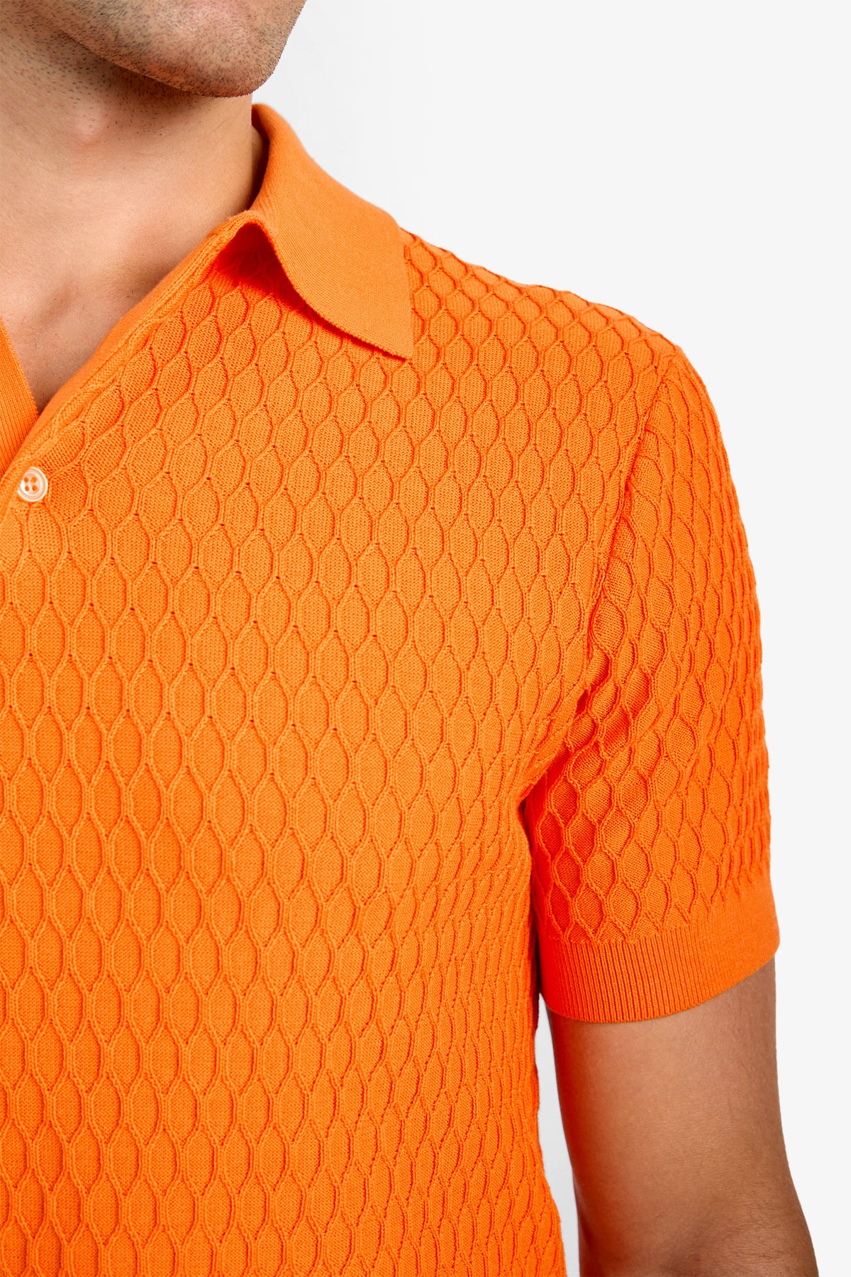 A person wearing the HONALO SS POLO, a textured short-sleeve bright orange 100% cotton collared shirt, is photographed from the shoulders up against a plain white background.