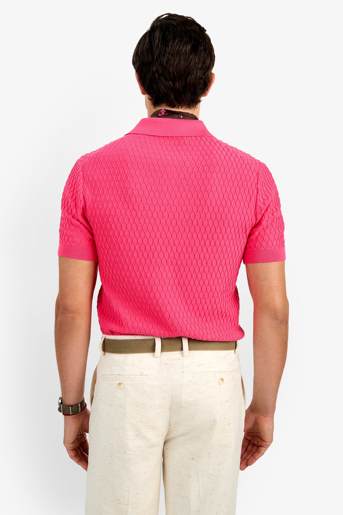 A man faces away, wearing the HONALO SS POLO—a textured pink short-sleeve 100% cotton shirt—paired with light beige trousers and a tan belt, set against a plain white background.