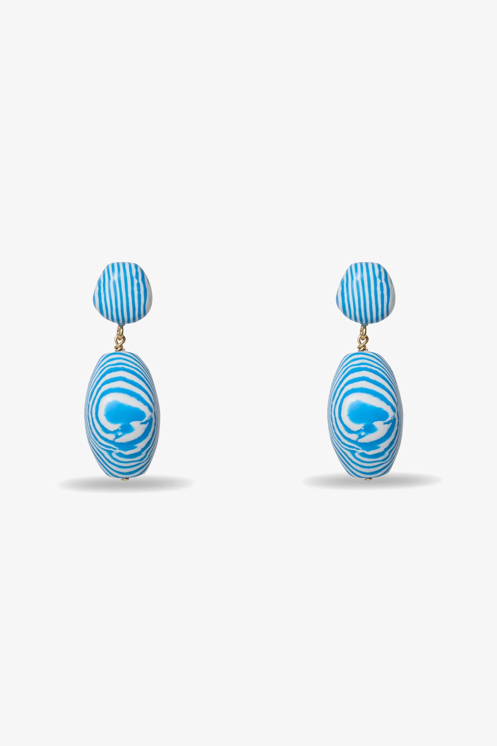 Ocean Baroque Double Drop Earrings feature blue and white abstract swirl patterns, with a small round stud and a larger oval drop. Both pieces display wavy lines and are shown on a plain light gray background.