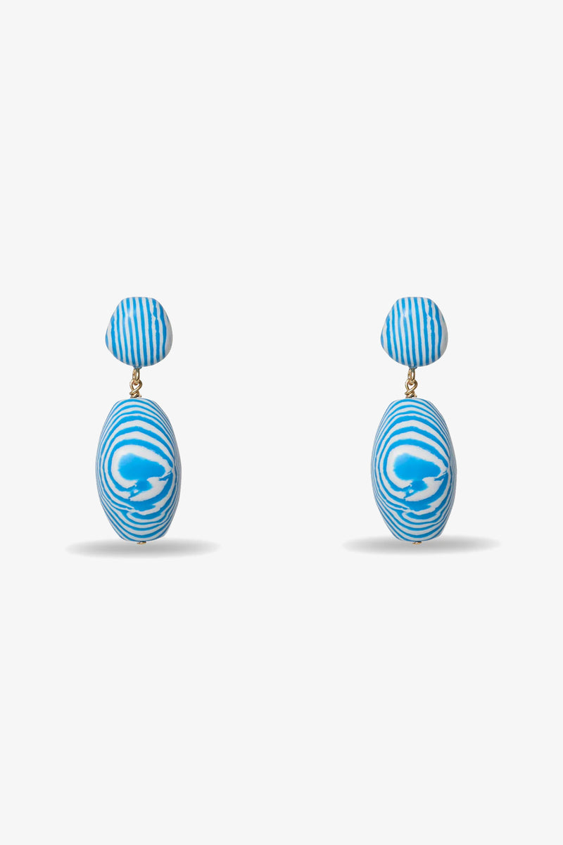 Ocean Baroque Double Drop Earrings feature blue and white abstract swirl patterns, with a small round stud and a larger oval drop. Both pieces display wavy lines and are shown on a plain light gray background.