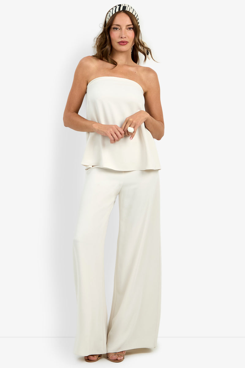 Woman wearing the Hulla Top, a strapless white top, paired with matching wide-leg pants and a black-and-white patterned headband, standing against a plain white background.
