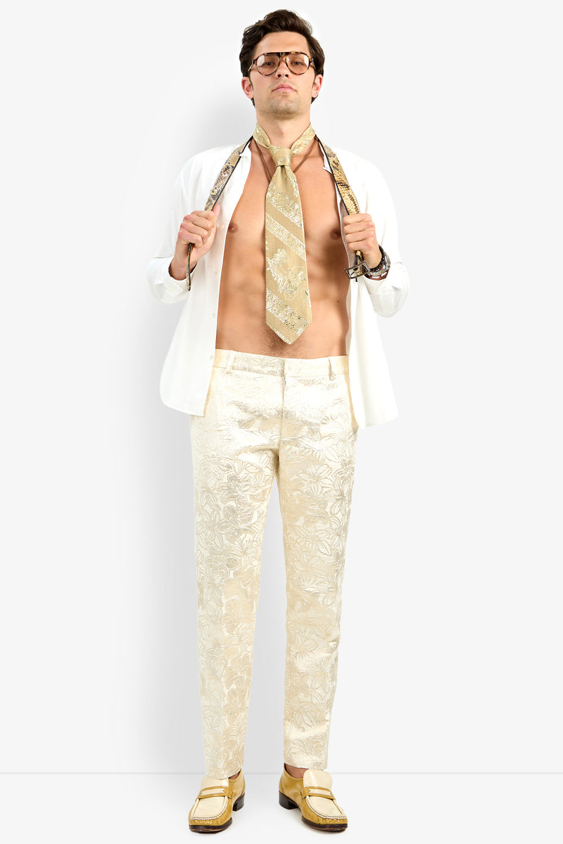 A man wears the Able Shirt open over patterned cream pants and gold loafers, showing his bare chest. He accessorizes with glasses and a printed tie, holding its ends confidently with both hands.