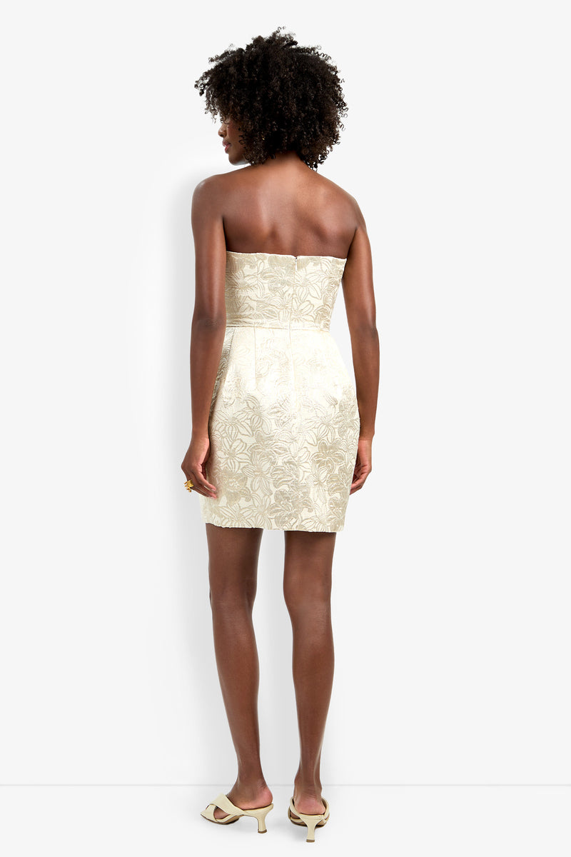 A woman with short curly hair stands with her back to the camera, wearing the strapless cream floral Kalley Dress paired with matching open-toe heels.