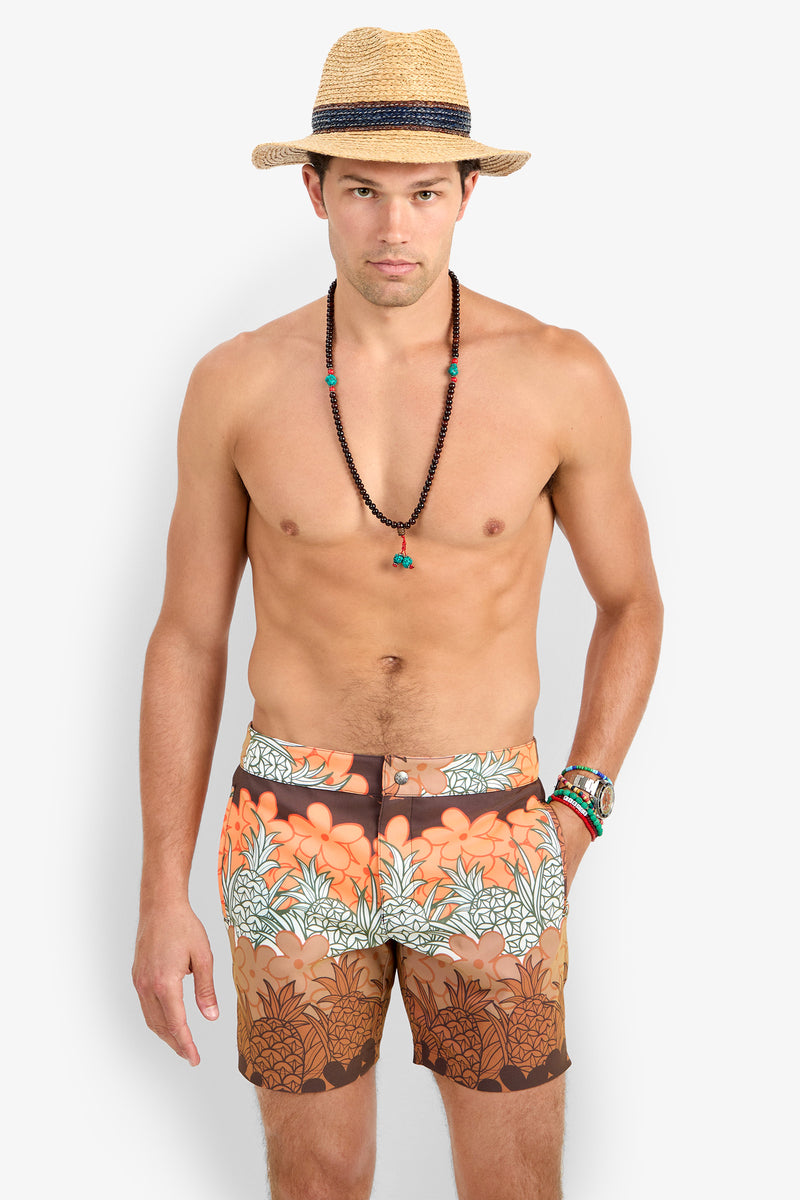 A man faces forward with a neutral expression, wearing the Honolulu Board Short and a straw hat with beaded necklaces, set against a plain white background.