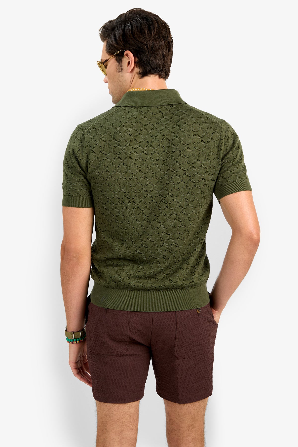 A man wearing the Waylen Short Sleeve Polo in olive green and brown textured shorts stands facing away with one hand in his pocket against a plain white background.