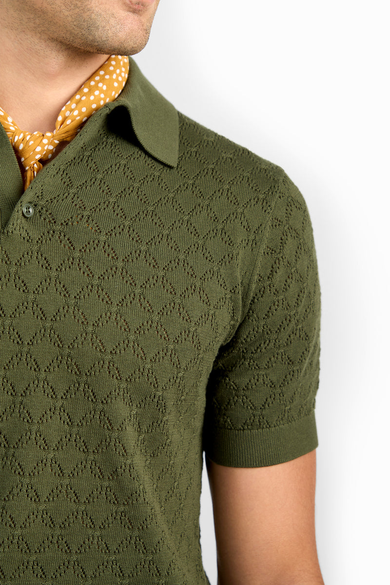 A person wearing the Waylen Short Sleeve Polo in olive green with a textured finish and collar, paired with a yellow polka-dot scarf around their neck, shown from the shoulders up against a white background.
