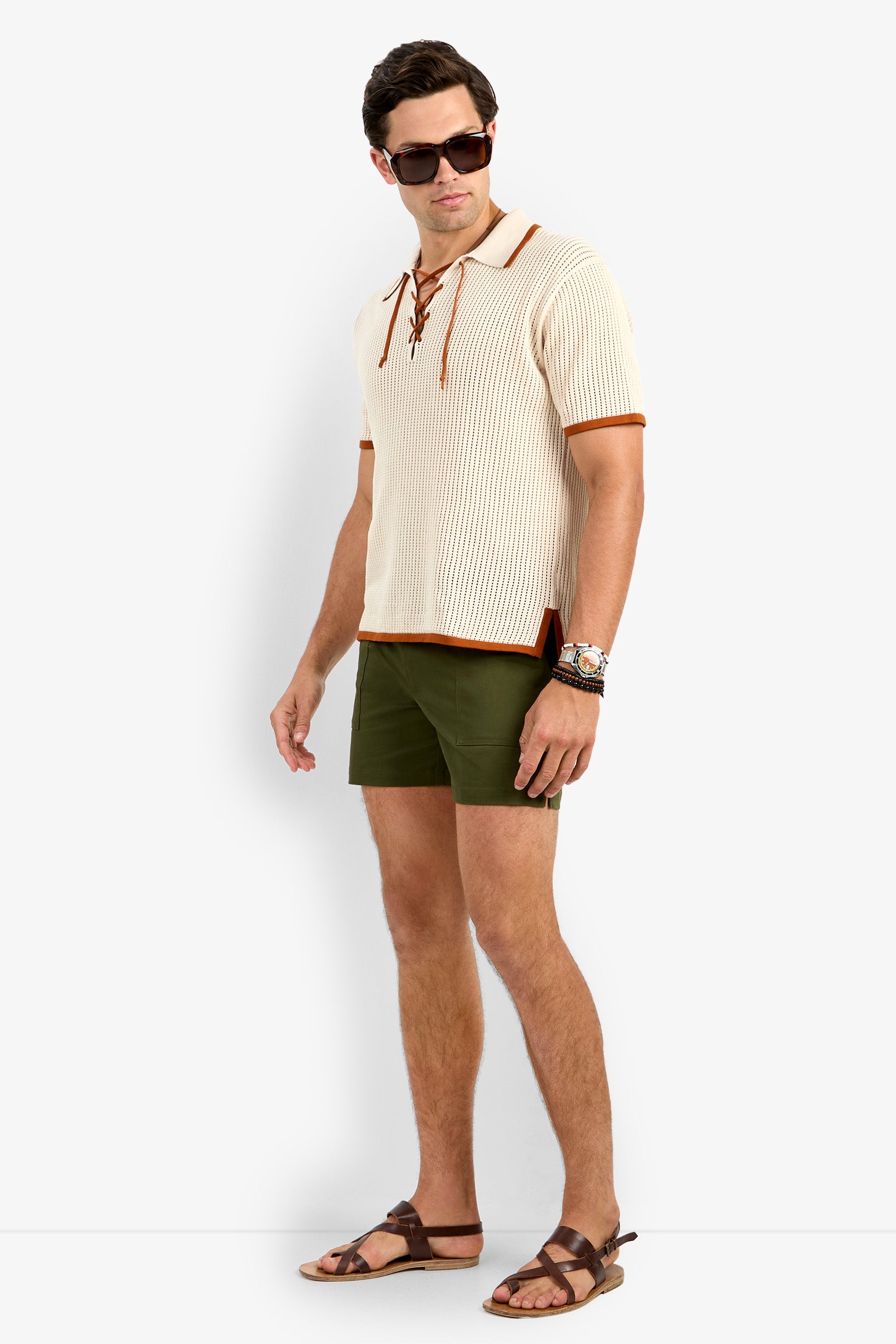 A man in sunglasses, olive green shorts, brown sandals, a watch, and the Simon Lace Up Polo stands against a plain white background.