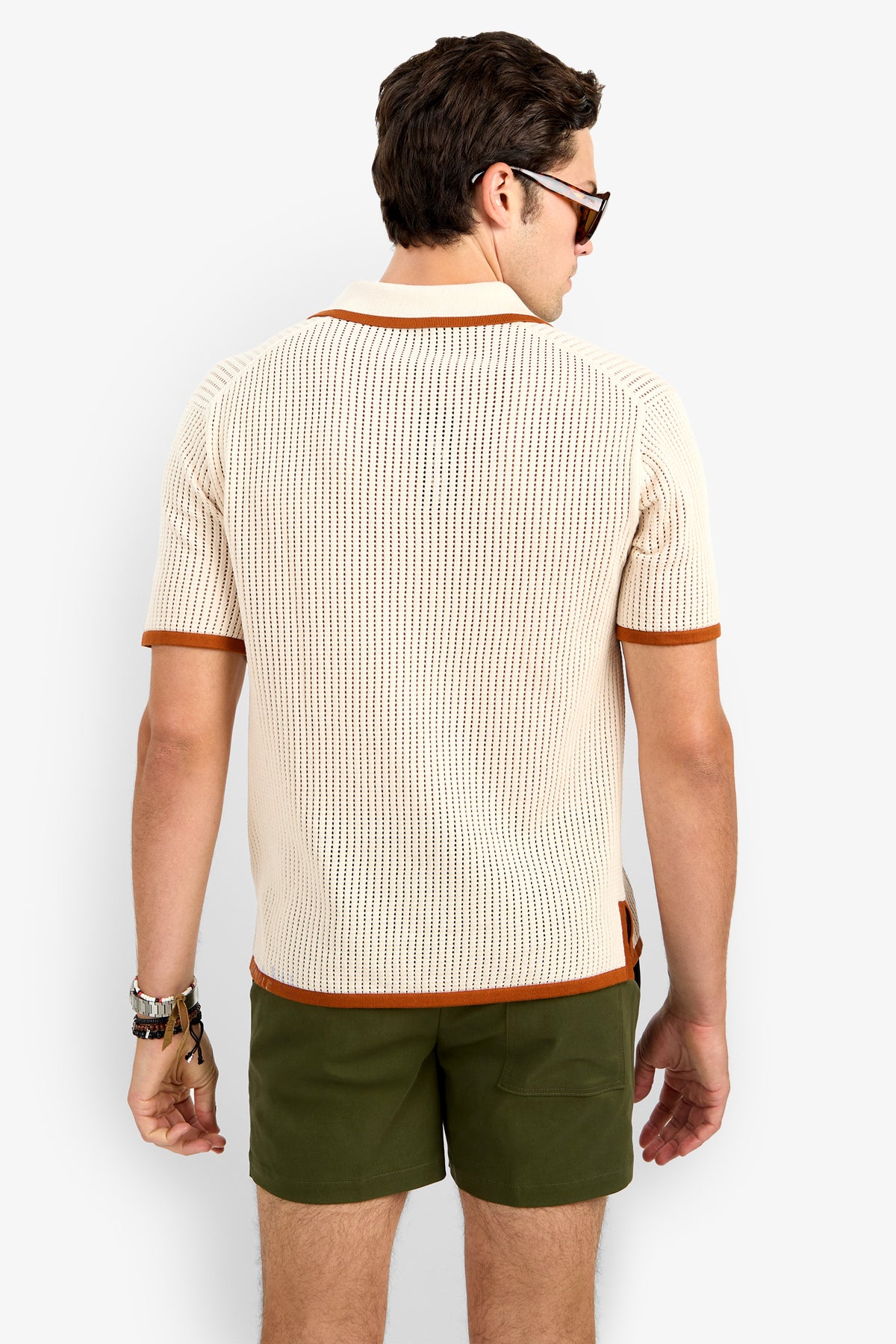 A man with short brown hair, wearing sunglasses and a Simon Lace Up Polo in beige with brown trim and green shorts, stands with his back to the camera against a plain white background.