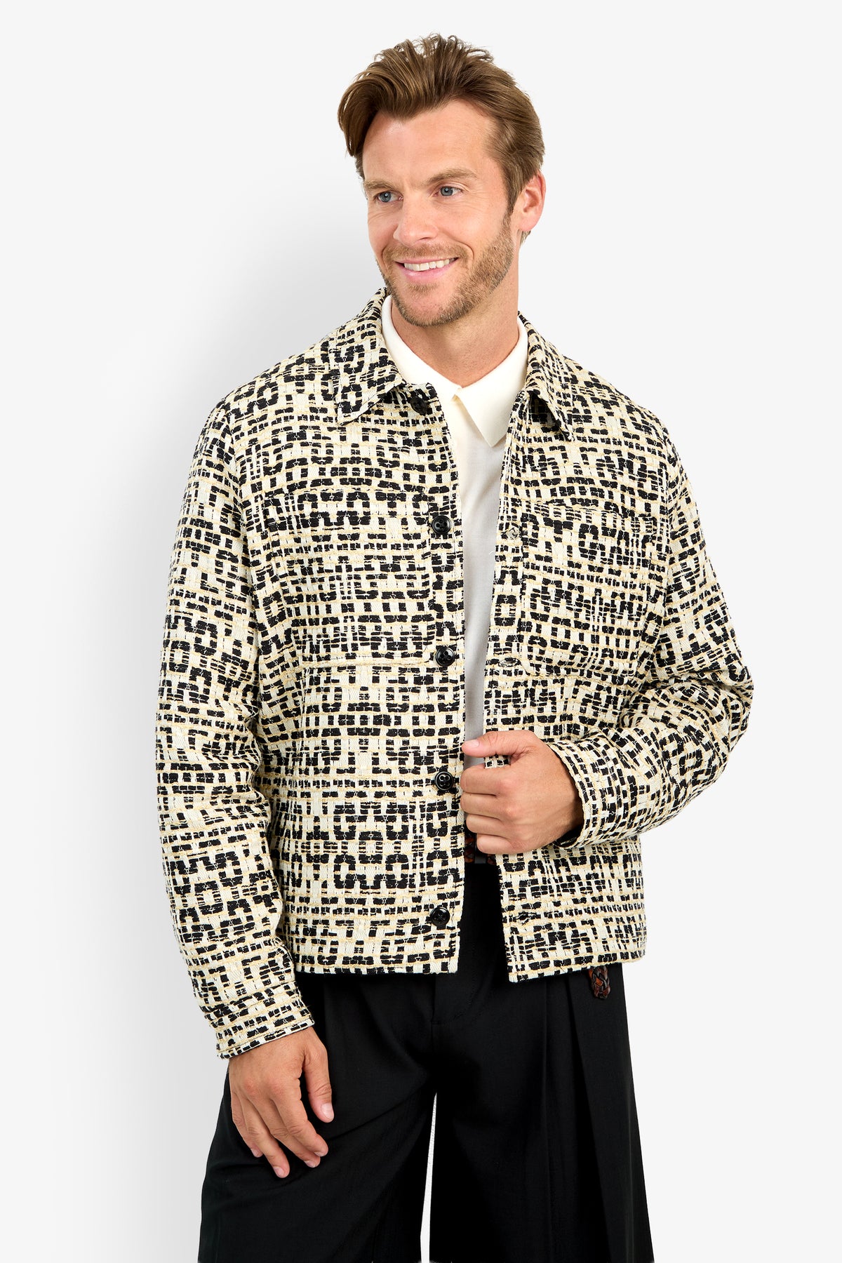 A man stands against a plain white background, smiling and holding his open PIERRE JACKET—featuring a cream and black pattern—over a white shirt.