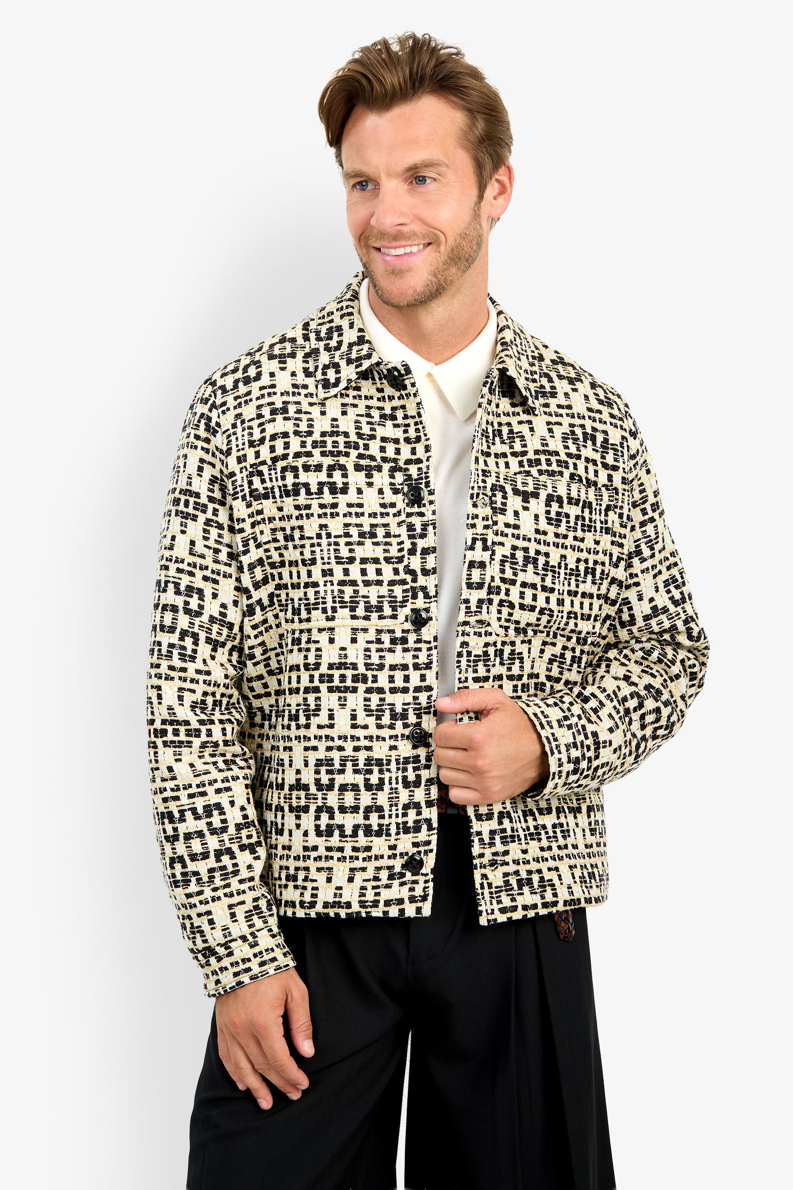 A man stands against a plain white background, smiling and holding his open PIERRE JACKET—featuring a cream and black pattern—over a white shirt.