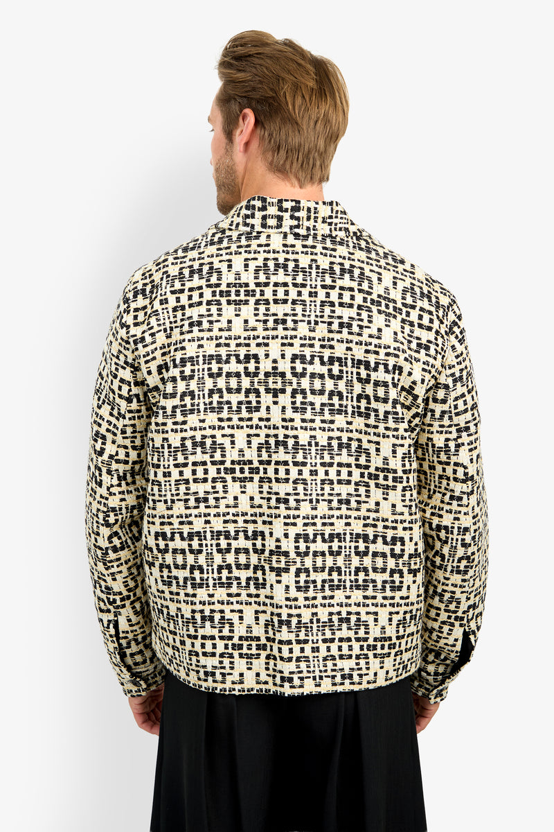 A man with light brown hair is seen from behind, wearing the PIERRE JACKET featuring a cream and black geometric pattern, standing against a plain white background.