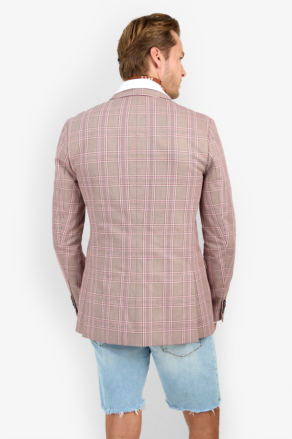 A man faces away wearing the THURSTON BLAZER in pink plaid over a white shirt and light blue frayed denim shorts, set against a plain white background.