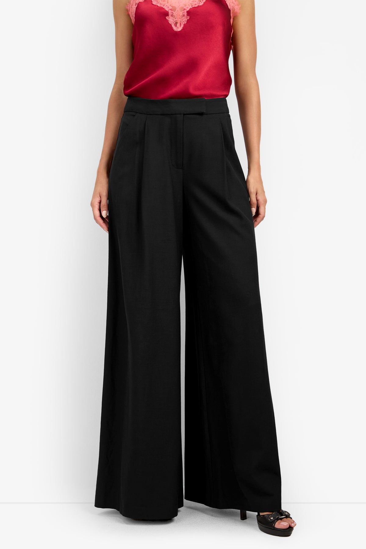 A person wearing a sleeveless red satin top with lace trim and high-waisted, wide-leg MIMMO PANT paired with black heels, standing against a white background.