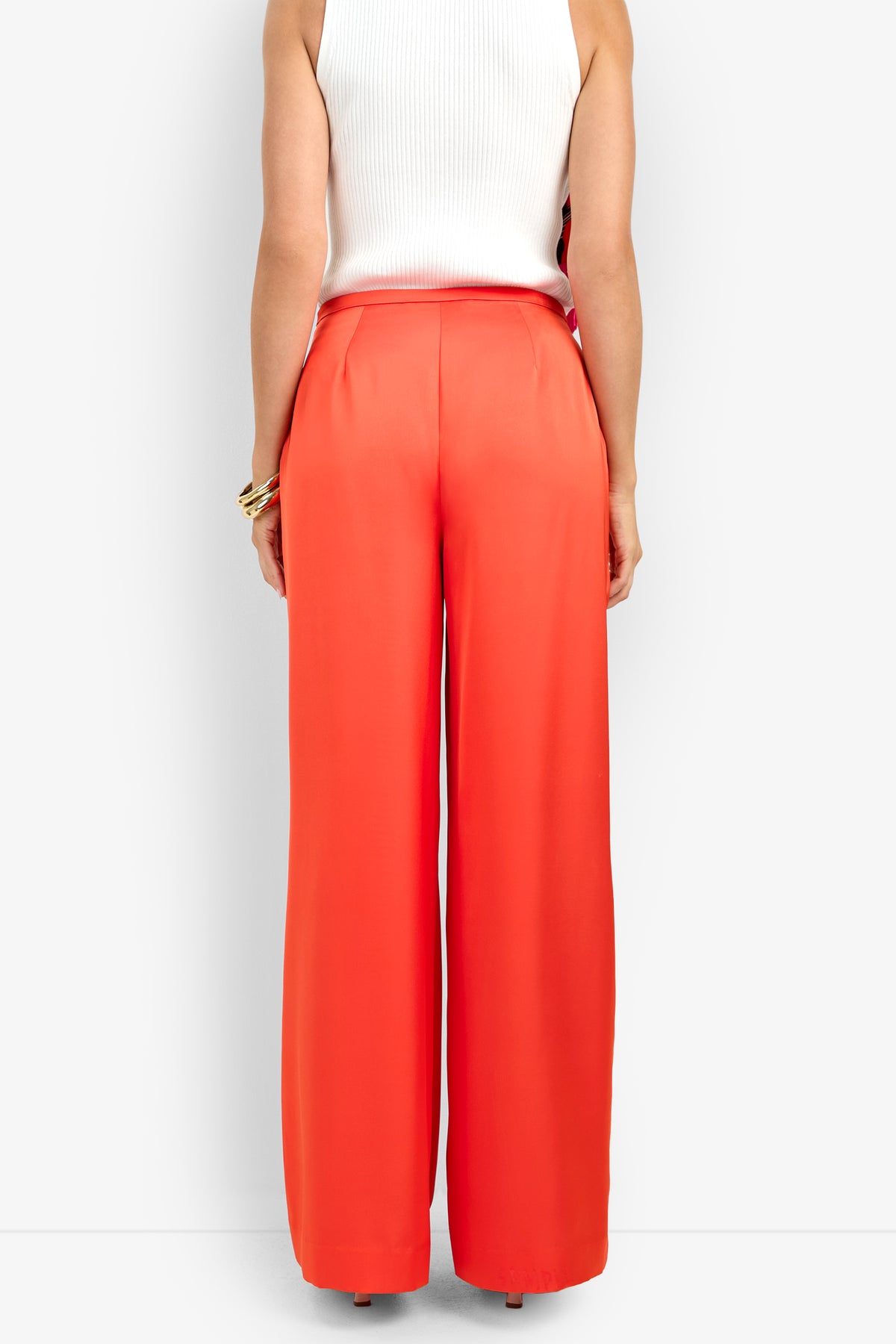 A person is shown from the back wearing the TAVIA PANT in bright orange with a white sleeveless top, standing against a plain white background.