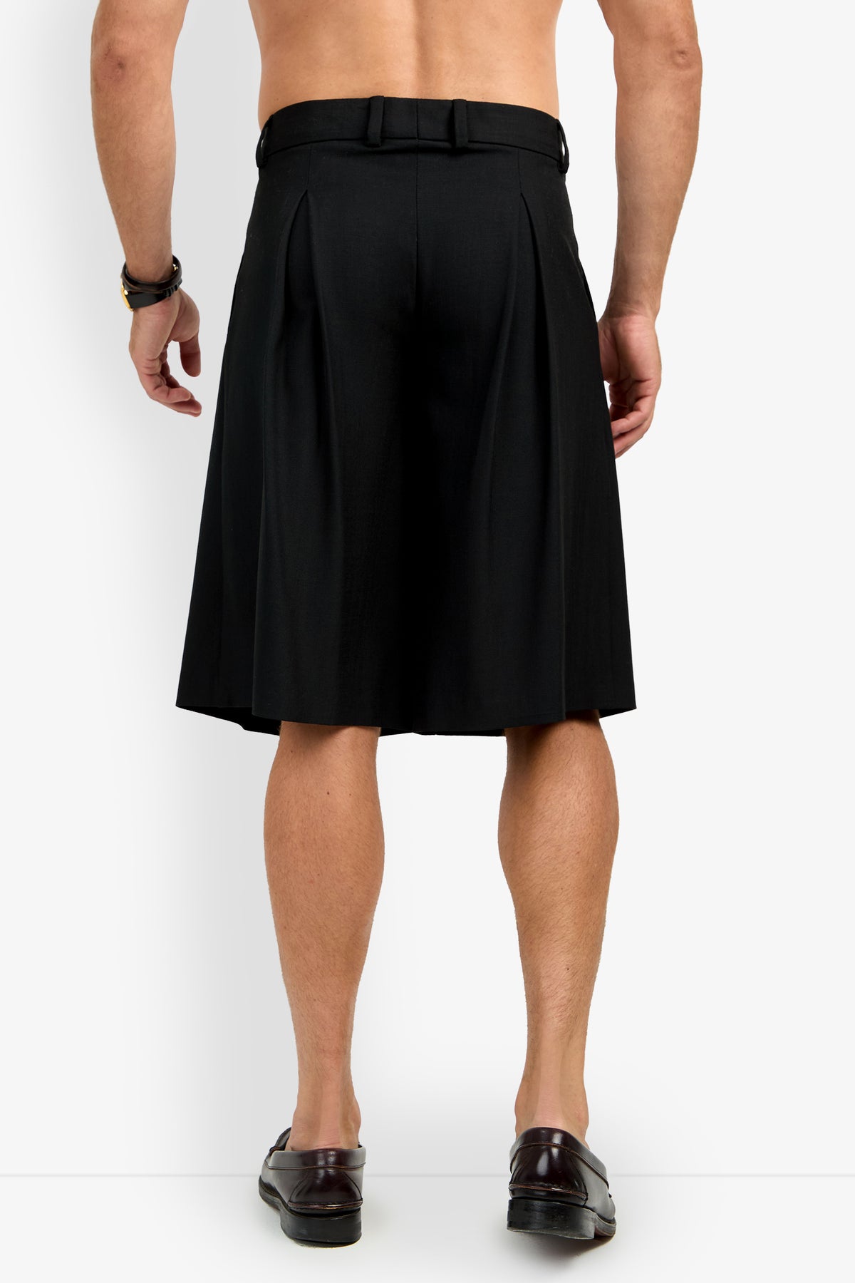 A shirtless man is shown from the back, wearing black GALFANO WIDE LEG SHORTS, a black belt, brown bracelet, and brown loafers, standing against a plain white background.