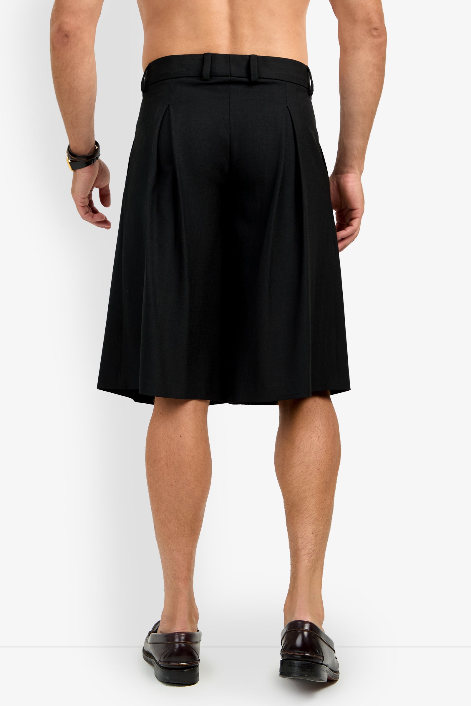 A shirtless man is shown from the back, wearing black GALFANO WIDE LEG SHORTS, a black belt, brown bracelet, and brown loafers, standing against a plain white background.