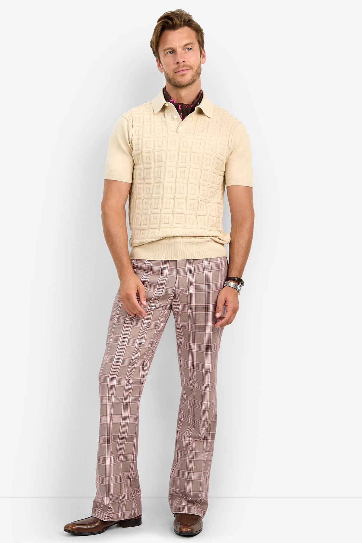 A man stands against a white background wearing a beige short-sleeve sweater, brown shoes, a watch, and the Alejandro Bootleg Trouser with one hand in his pocket.