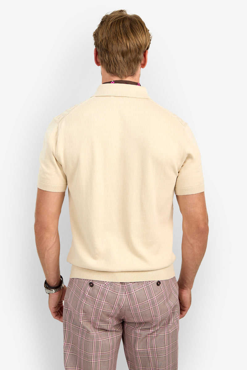 A man with light brown hair is seen from behind, wearing the VERNON POLO in beige and pink plaid pants. He has a watch on his left wrist and stands in front of a plain, light background.